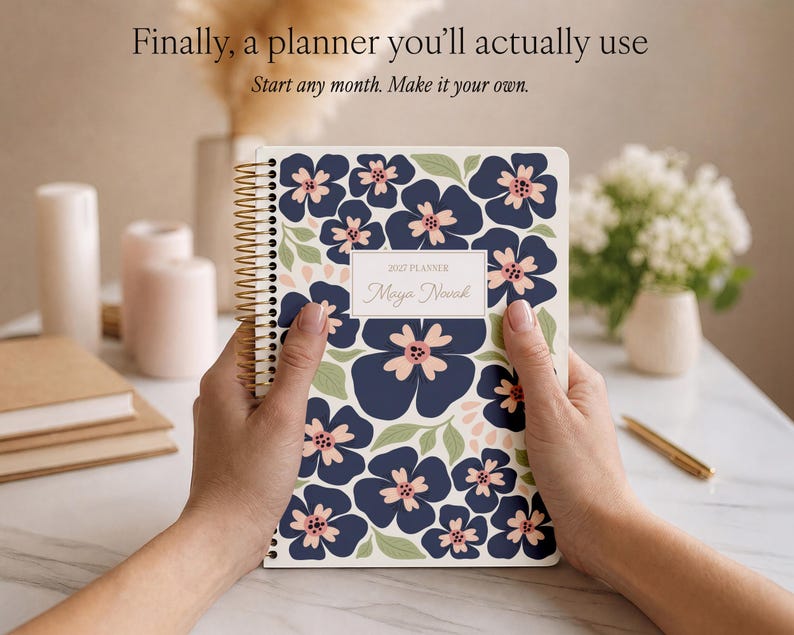 May include: A spiral-bound 2027 planner with a dark blue floral pattern on a white background. The cover features a central rectangular label with the text 2027 PLANNER and Maya Novak. The planner has gold-toned wire binding along the left side.