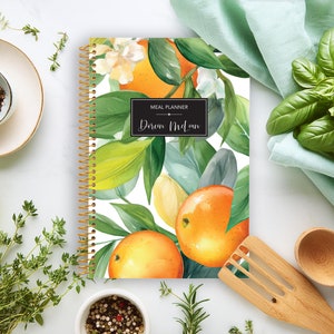 May include: A white meal planner with a spiral binding. The cover features a watercolor illustration of orange blossoms and leaves. The text "Meal Planner" and "Doren McLean" is printed on the cover.