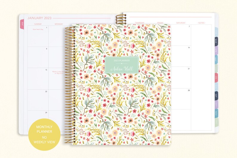 8.5x11" Posy Paper Co. 2023/2024 monthly planner with the meadow floral cover design showcasing 2 page monthly spread layout in the background.