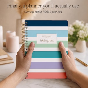 Puede incluir: Una agenda 2027 de espiral con rayas horizontales en azul marino, azul claro, verde, cerceta, lavanda, blanco y coral. La portada incluye una etiqueta rectangular blanca con el texto 2027 PLANNER y Whitney Hicks.