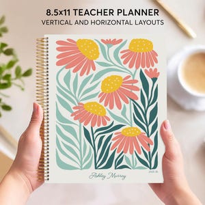 May include: An 8.5x11 inch teacher planner with a floral design featuring pink and yellow flowers on a white background. The planner has a gold spiral binding and the text "Ashley Murray" and "2023-24" printed on the cover.