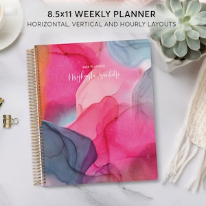 May include: A pink, blue, and gray abstract design covers the front of a 8.5x11 weekly planner. The planner has a gold wire-o binding and the text "2024 Planner" and "Myfaula Santillo" are printed on the cover.