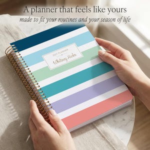 Puede incluir: Una agenda 2027 de espiral con rayas horizontales en azul marino, azul claro, verde menta, cerceta, lavanda y coral. Una etiqueta rectangular blanca en la portada presenta el texto 2027 PLANNER y el nombre Whitney Hicks en letra cursiva.