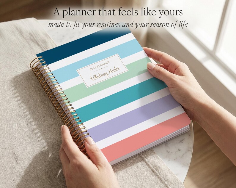 Puede incluir: Una agenda 2027 de espiral con rayas horizontales en azul marino, azul claro, verde menta, cerceta, lavanda y coral. Una etiqueta rectangular blanca en la portada presenta el texto 2027 PLANNER y el nombre Whitney Hicks en letra cursiva.