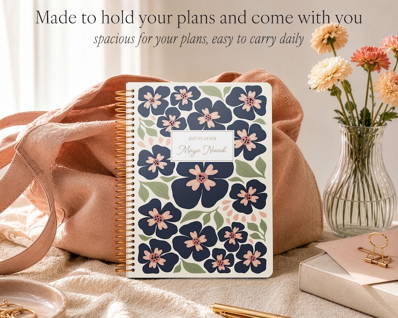 May include: A spiral-bound 2025 planner with a white cover featuring a dark blue and light pink floral pattern and green leaves. The center label reads 2025 PLANNER and Maya Novak. The text above the planner reads Made to hold your plans and come with you, spacious for your plans, easy to carry daily.