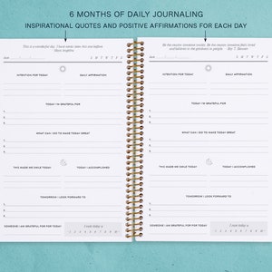 May include: A white journal with a gold spiral binding. The journal is divided into sections for daily journaling, including "Today I'm Grateful For", "What Can I Do To Make Today Great", "This Made Me Smile Today", "Today I Accomplished", "Tomorrow I Look Forward To", and "Someone I Am Grateful For Today". The journal also includes inspirational quotes and positive affirmations for each day.