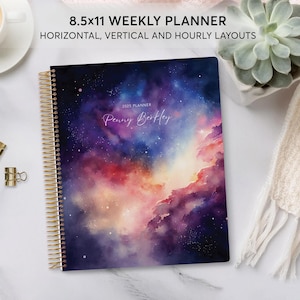 May include: An 8.5x11 weekly planner with a watercolour galaxy design. The planner cover features a purple, pink, and blue nebula with a gold spiral binding. The text "2023 Planner" and "Penny Berkley" are printed on the cover.