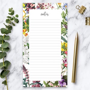 May include: Floral notepad with a white background and lined paper. The border is decorated with a variety of colourful flowers, including purple, pink, yellow, and white.