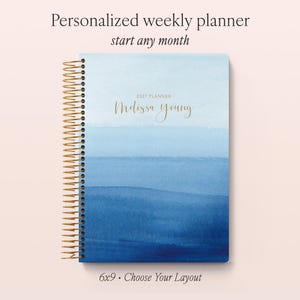 May include: A weekly planner with a gold spiral binding and a blue watercolour gradient cover. The cover features the text 2027 PLANNER and the name Melissa Young in gold script. The planner measures 6x9 inches and includes a customisable layout.