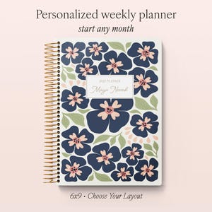 May include: A spiral-bound weekly planner with a white cover featuring a dark blue floral pattern with light pink centres and sage green leaves. A central rectangular label displays the text 2017 PLANNER and the name Maya Novak in script.