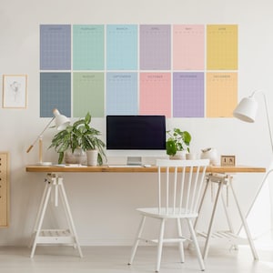 Peut inclure: Un bureau blanc avec un plateau en bois et des pieds en tréteau blancs. Une chaise blanche est placée devant le bureau. Un écran d'ordinateur, deux lampes et des plantes sont sur le bureau. Un calendrier avec 12 mois est affiché au mur derrière le bureau. Le calendrier est de couleur pastel et présente un motif en grille.