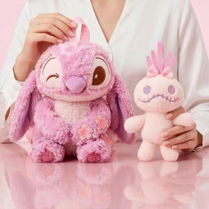 Puede incluir: Se muestran dos peluches rosas. Uno es un personaje grande y esponjoso con orejas grandes, un ojo gui&ntilde;ado y detalles florales. El otro es una mu&ntilde;eca m&aacute;s peque&ntilde;a, de color rosa claro, con rasgos cosidos y un lazo.