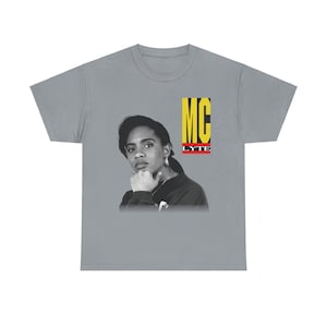 Op de afbeelding: Een grijs T-shirt met een zwart-wit afbeelding van MC Lyte. De tekst "MC Lyte" is in gele en rode letters.
