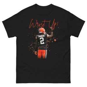 Puede incluir: Una camiseta negra de manga corta con el gráfico de un jugador de fútbol americano que lleva una camiseta negra con el nombre SANDERS y el número 2 en la espalda. El jugador tiene un brazo levantado y el texto Wrist Up! en color naranja.