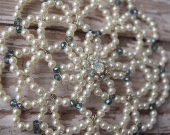 May include: A white beaded kippah with a blue rhinestone in the center. The kippah is made of small, round pearls and has a delicate, intricate design.