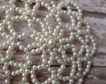 May include: A white pearl and crystal beaded hair accessory with a gold center piece.