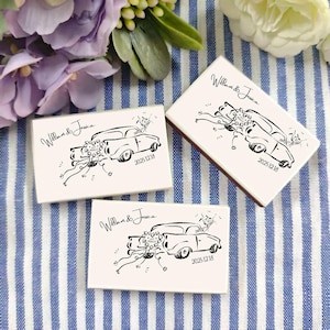 May include: Three rectangular, off-white boxes with a black line drawing of a vintage car decorated with flowers and ribbons. The text "William & Jessica" and the date "2025.12.18" are also printed on the boxes. The boxes are on a blue and white striped surface.