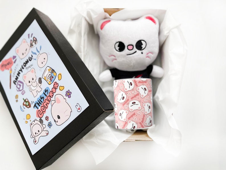 K&ouml;nnte beinhalten: Eine schwarze Box mit einem blauen und wei&szlig;en Design, das eine Comic-Katze und den Text "This is Comprox" und "Annyeong!" zeigt. Die Box ist ge&ouml;ffnet und im Inneren befindet sich ein wei&szlig;es Pl&uuml;schkatzenspielzeug mit einem schwarzen Shirt und eine wei&szlig;e Tasse mit einem rosa-wei&szlig;en Comic-Katzenmuster.