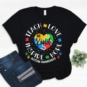 May include: Black t-shirt with a colourful puzzle piece heart and the text "Teach Love Inspire Hope Autism Awareness" in white.