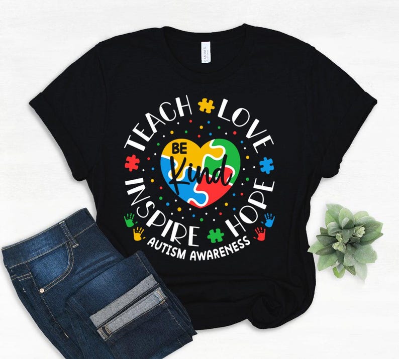 May include: Black t-shirt with a colourful puzzle piece heart and the text "Teach Love Inspire Hope Autism Awareness" in white.