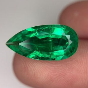 May include: A pear-shaped, faceted gemstone with a vibrant, translucent green color. The stone features a pointed end and a rounded base, with internal light reflections visible across its polished surface, showcasing a clear, brilliant emerald hue.