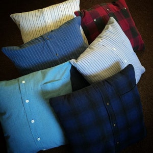 May include: Six pillows made from repurposed shirts. The pillows are in various colors and patterns, including blue, white, red, and black.