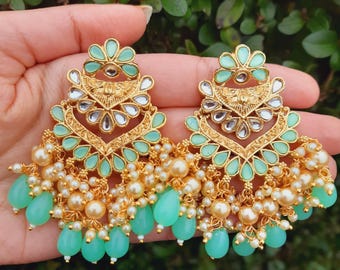 May include: A pair of gold earrings with a mint green and white design. The earrings feature a teardrop shape with a beaded fringe and a floral design at the top.