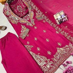 May include: A vibrant fuchsia-colored salwar kameez ensemble. The tunic and pants are made of a smooth fabric, with intricate gold and silver embroidery along the neckline, sleeves, and hem. A matching sheer dupatta is included.