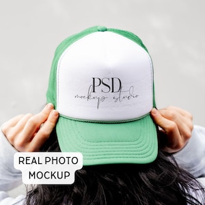 May include: A green and white trucker cap featuring a white front panel with the black text PSD mockup studio printed in the centre. The cap has a green brim, a green mesh back, and a green cord detail running across the base of the front panel.
