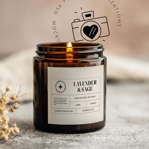 May include: A lit brown glass jar candle with a white label that reads "Lavender & Sage." The candle is part of the "Classic Collection" and made with 100% natural soy wax. The candle has a burn time of 50-60 hours.