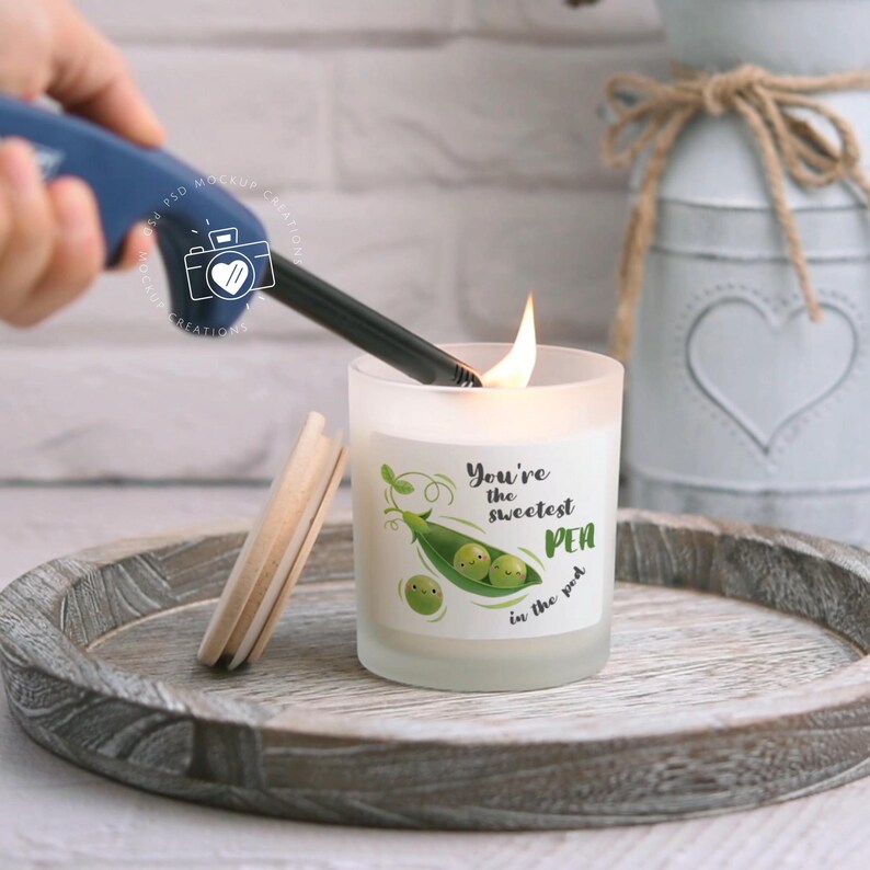 May include: A white frosted glass candle with a wood lid. The candle has a label that says "You're the sweetest pea in the pod" with a green pea pod and three peas with faces.