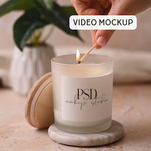 Może przedstawiać: Zapalone świeca w mrożonym szklanym słoiku z białą etykietą z napisem "PSD mockup studio". Świeca stoi na małym, okrągłym, marmurowym spodku. Drewniana pokrywka spoczywa obok świecy. Ręka zapala świecę zapałką. Słowa "VIDEO MOCKUP" znajdują się w białym prostokącie.