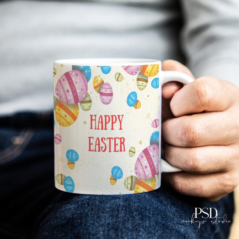 May include: White ceramic mug with a colorful Easter egg pattern and the words "HAPPY EASTER" in red. The eggs are decorated with stripes and stars in shades of pink, yellow, and blue. The mug is held by a person.