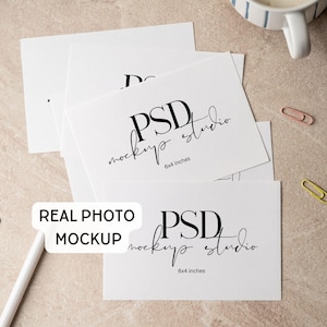 May include: A stack of white rectangular cards with the black text PSD mockup studio and 6x4 inches printed on them. A white stylus, a blue push pin, and three paper clips in pink, yellow, and silver are scattered around the cards.