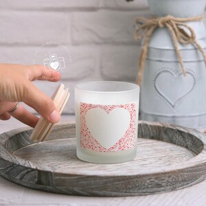 May include: A frosted glass candle jar with a white heart design surrounded by red dots. The candle jar is on a wooden tray.