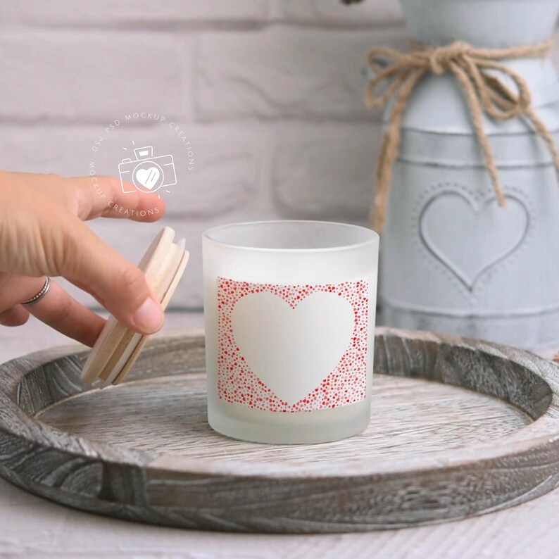 May include: A frosted glass candle jar with a white heart design surrounded by red dots. The candle jar is on a wooden tray.
