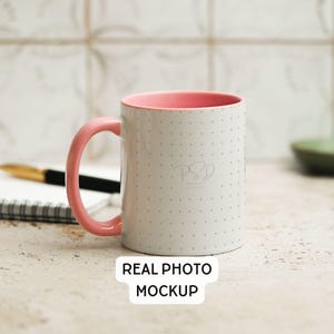 May include: White ceramic mug with a pink interior and handle. The mug has a dotted pattern and the text "PSD" in a script font. The words "REAL PHOTO MOCKUP" are at the bottom of the image.