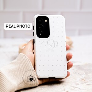 May include: White phone case with a small white polka dot pattern. The case has a black camera lens cutout and the text "PSD Mock Up Creations" in gray.