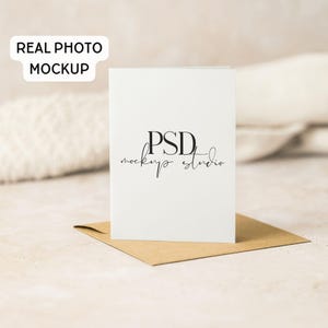 May include: A white folded card with the text "PSD mockups studio" in black script, resting on a brown envelope. The words "REAL PHOTO MOCKUP" are in a white rectangle in the upper left corner.