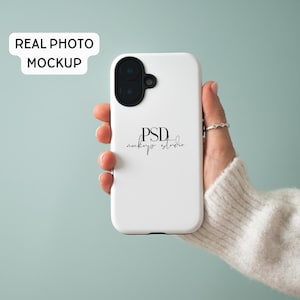 May include: A white phone case with a black camera module is held in a hand. The case has the text "PSD mockups studio" in a script font. The words "REAL PHOTO MOCKUP" are in a white rectangle in the upper left corner.