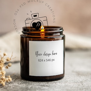 May include: A brown glass jar candle with a white label that says "Your design here" and the dimensions 624 x 546 px. A line drawing of a camera with a heart is above the jar. The candle is lit.