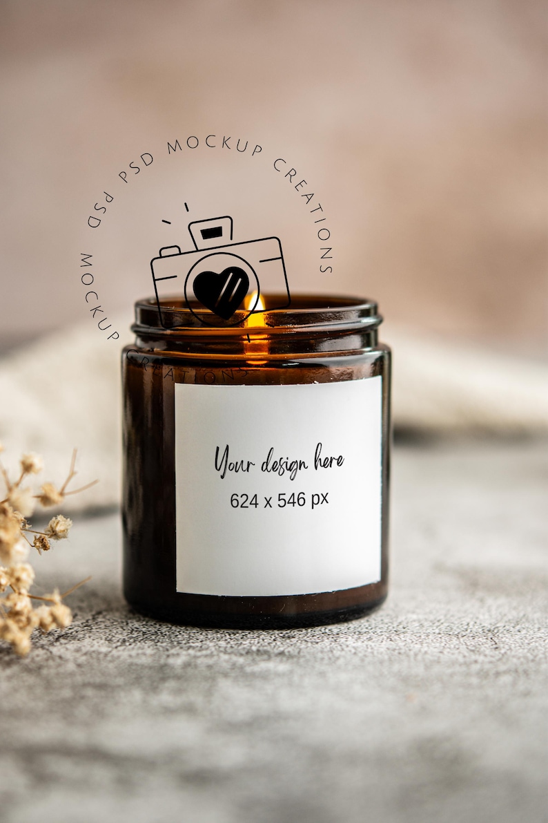 May include: A brown glass jar candle with a white label that says "Your design here" and the dimensions 624 x 546 px. A line drawing of a camera with a heart is above the jar. The candle is lit.