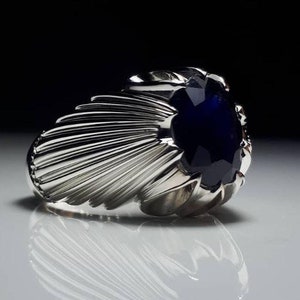 May include: A silver ring with a large, dark blue gemstone set in a fan-shaped design.
