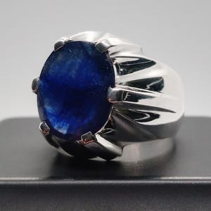 May include: A silver ring featuring a large, oval-cut, deep blue gemstone. The ring has a polished, ridged band and prongs that secure the stone. The gemstone's color is a rich, saturated blue.