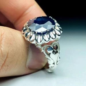 Peut inclure: Gros plan d'une bague en argent ornée d'une grosse pierre précieuse bleu foncé à facettes. La bague a un sertissage orné d'inspiration florale avec des détails complexes.