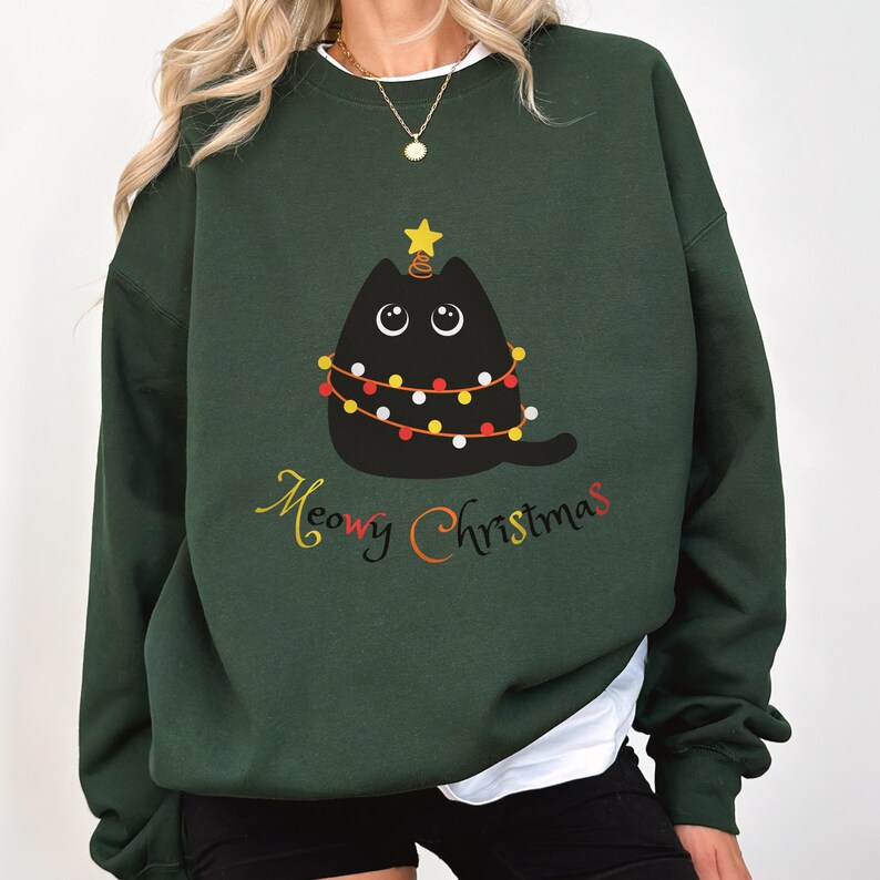 May include: A dark green sweatshirt with a black cat wearing a Christmas lights garland on its head. The text "Meow Christmas" is printed below the cat.