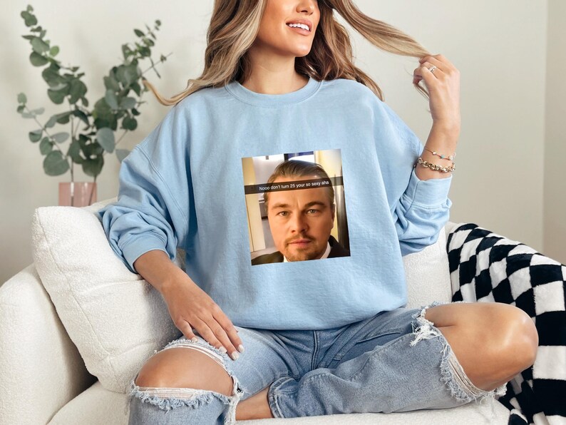 May include: A light blue sweatshirt with a graphic of Leonardo DiCaprio's face and the text "How don't I turn 15 if you're so very old".