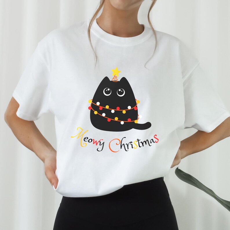 May include: White t-shirt with a black cat wearing Christmas lights and a star on its head. The text "Meowy Christmas" is printed below the cat.