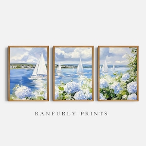 Puede incluir: Conjunto de tres impresiones artísticas enmarcadas que representan veleros en un mar azul, nubes blancas y flores de hortensia azules. La obra de arte tiene un marco de madera. El texto "RANFURLY PRINTS" está en la parte inferior.