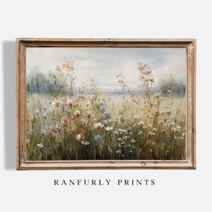 Op de afbeelding: Een ingelijst landschapsschilderij met een veld vol wilde bloemen in roze, blauwe, gele en witte tinten. Het kunstwerk is geplaatst tegen een zachte, bewolkte lucht en is ingelijst in een lichtbruine houten lijst. De tekst "RANFURLY PRINTS" staat onderaan.